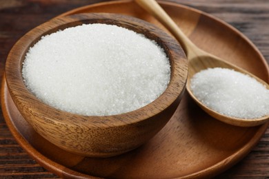 Photo of Granulated sugar in bowl and spoon on wooden table, closeup