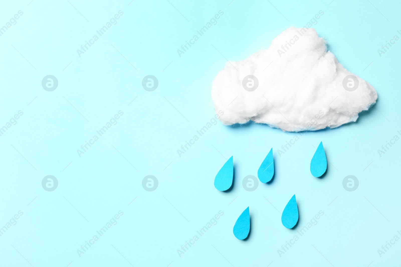 Photo of White cotton cloud and paper drops imitating rain on cyan background, flat lay. Space for text