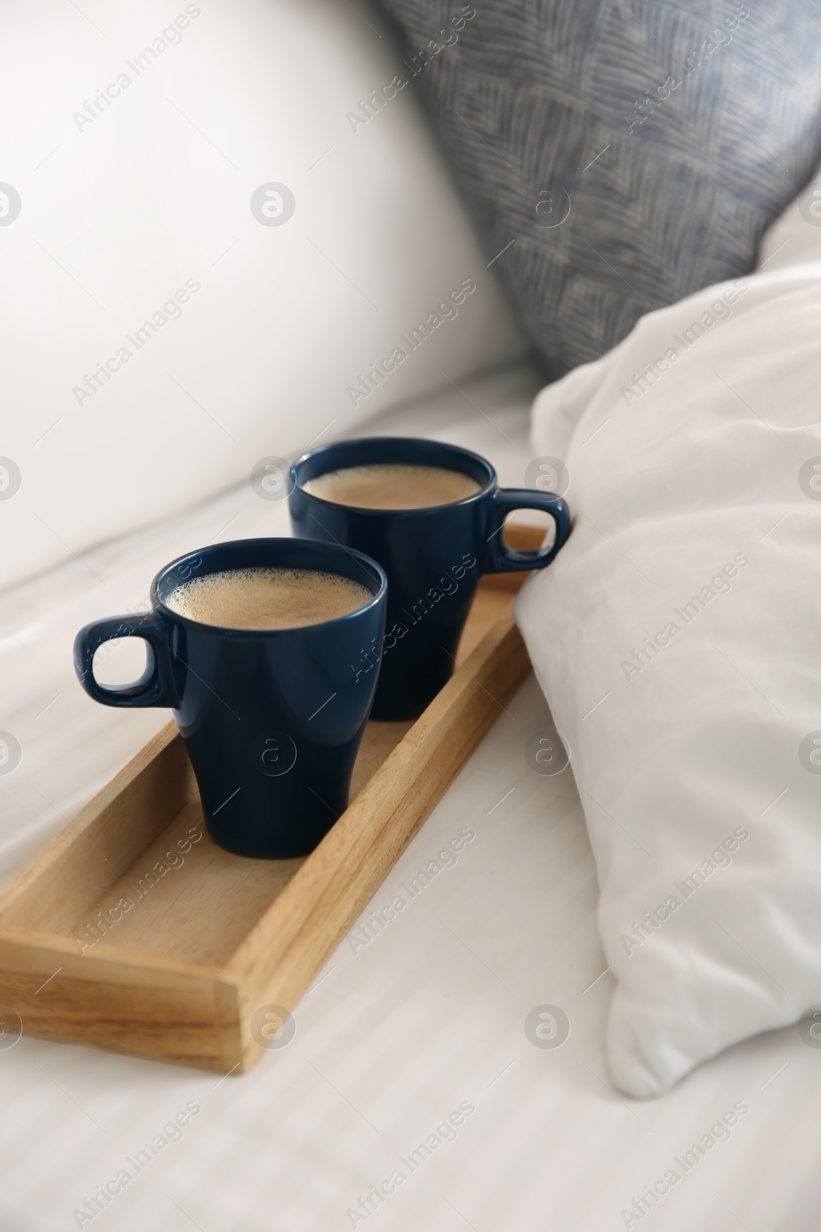 Photo of Wooden tray with cups of coffee near soft blanket on bed