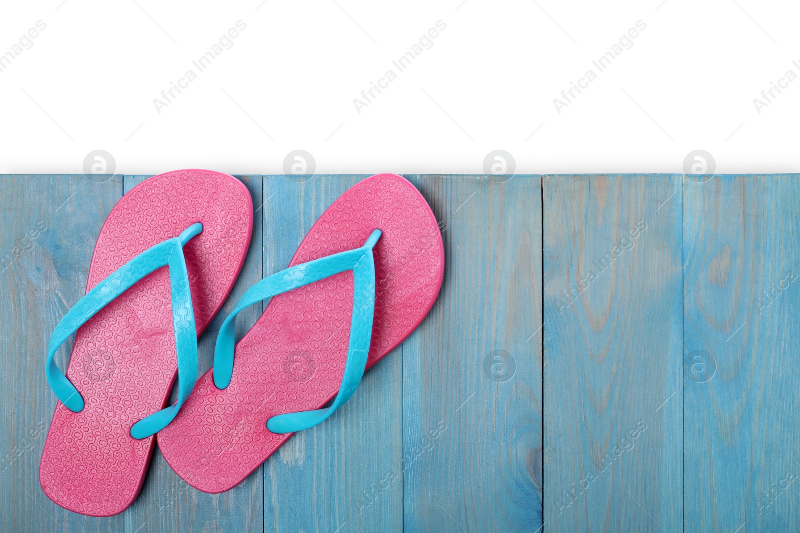 Photo of Pink flip flops and space for text on turquoise wooden table against white background, top view