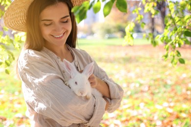 Woman holding cute white rabbit in park, space for text