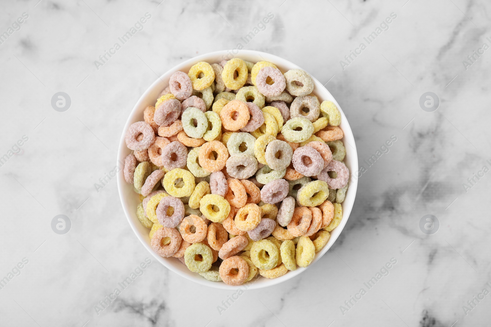 Photo of Tasty cereal rings in bowl on white marble table, top view