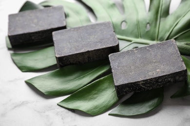 Photo of Natural tar soap and green leaf on white marble table, closeup