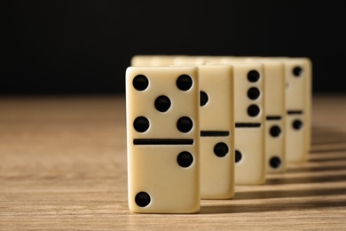 Photo of Domino tiles on wooden table against black background, closeup