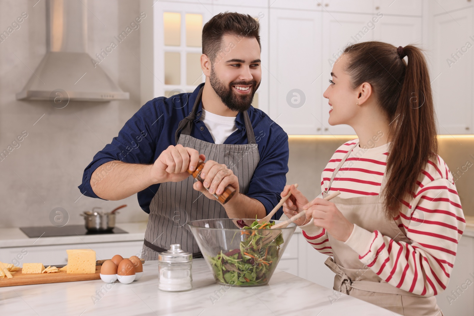 Photo of Happy affectionate couple cooking together at white table in kitchen