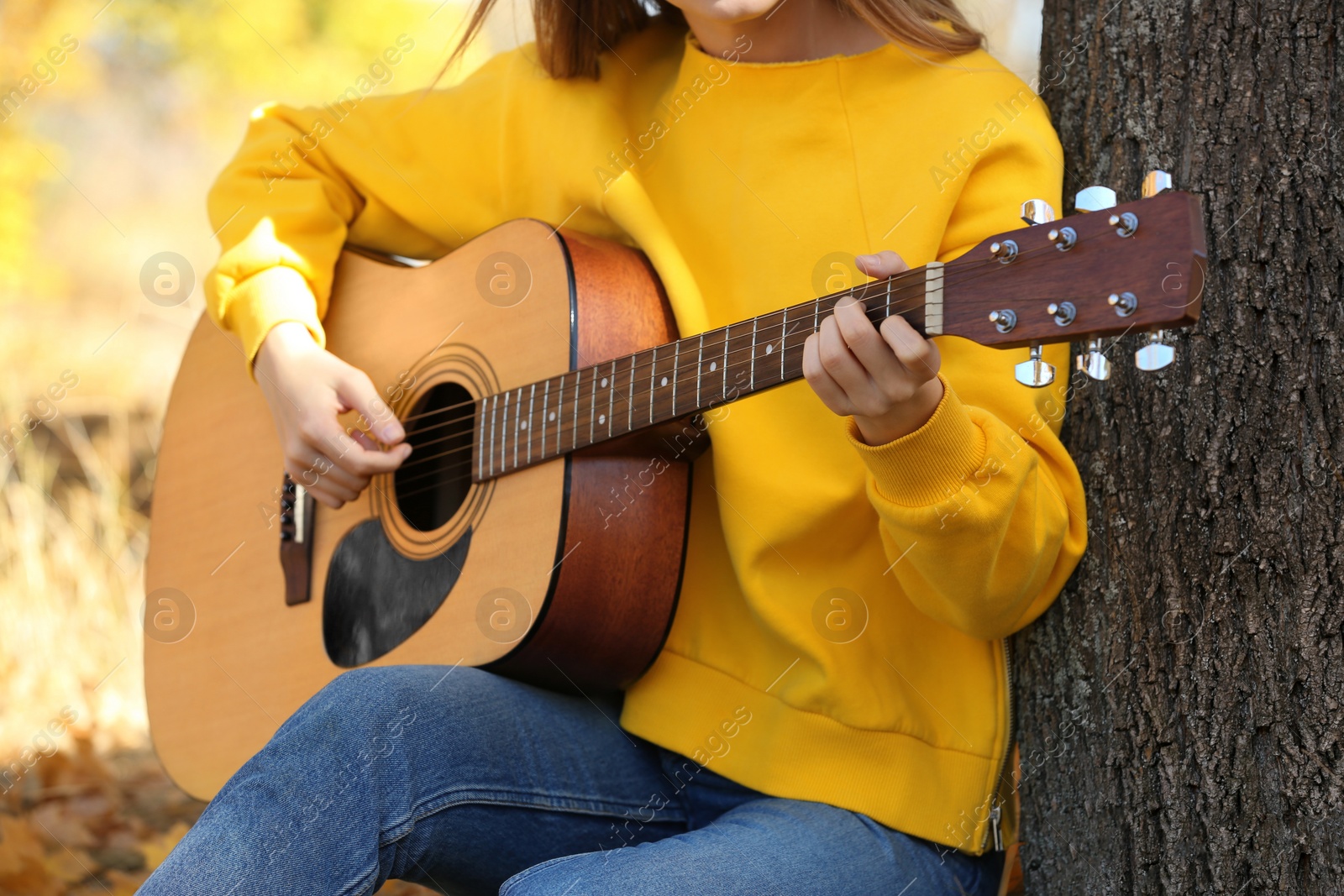 Photo of Teen girl playing guitar in autumn park, closeup