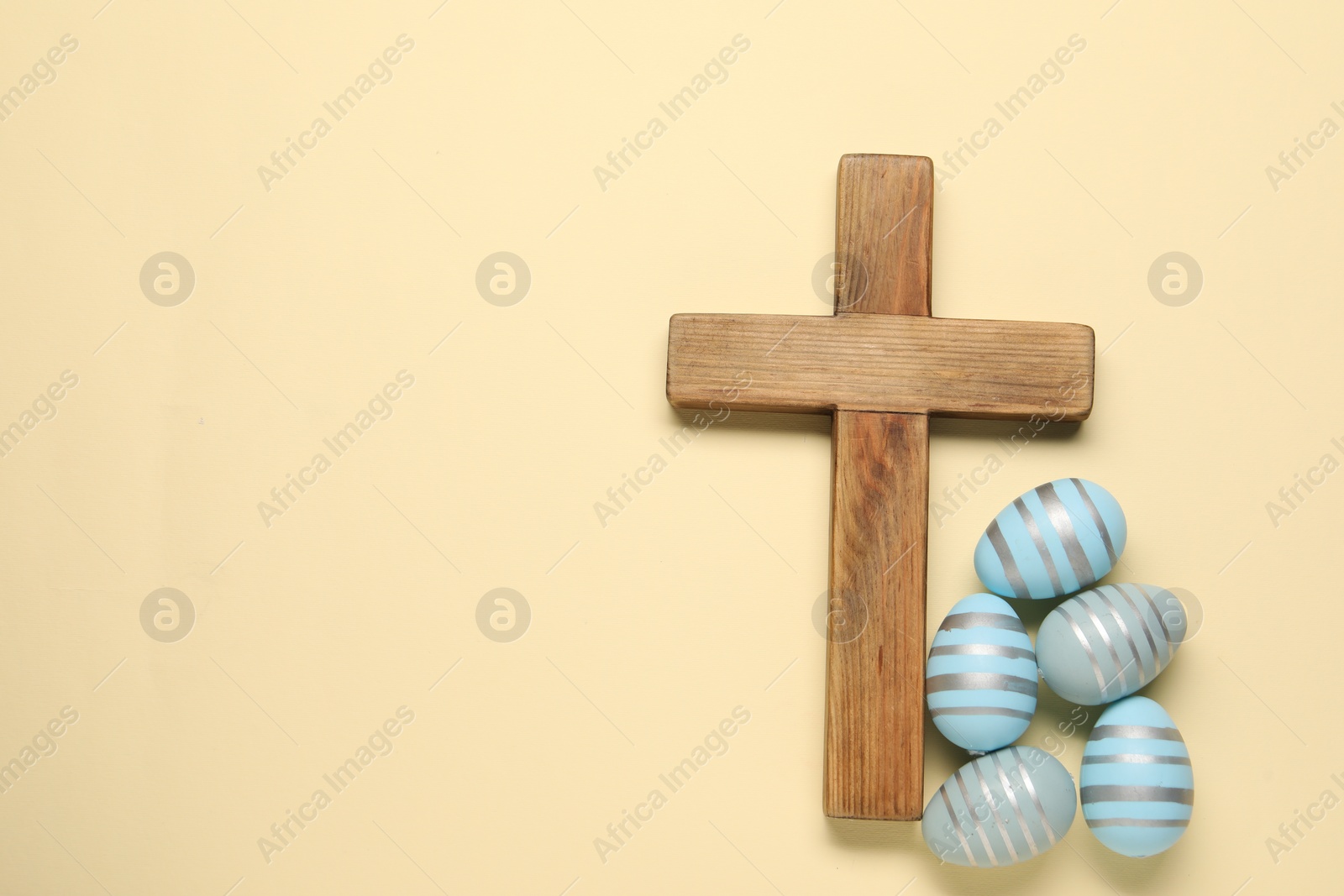 Photo of Wooden cross and painted Easter eggs on beige background, flat lay. Space for text