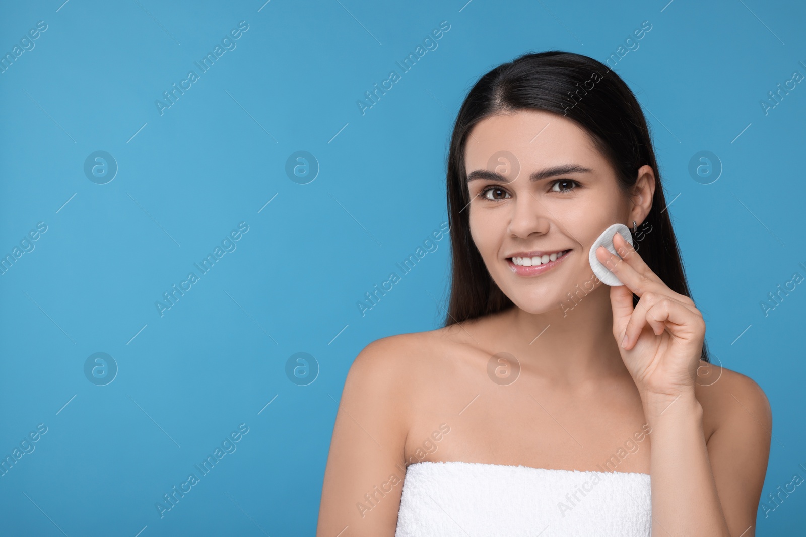 Photo of Young woman with cotton pad on light blue background. Space for text