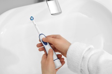 Photo of Woman turning on electric toothbrush above sink in bathroom, closeup