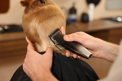 Professional hairdresser cutting boy's hair in beauty salon, closeup