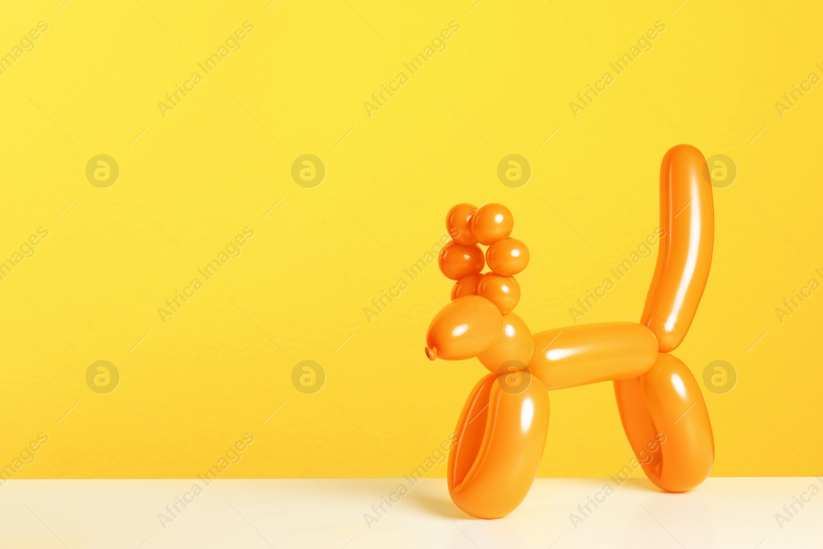 Photo of Animal figure made of modelling balloon on table against color background. Space for text