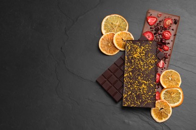 Photo of Different chocolate bars with freeze dried fruits on slate table, flat lay. Space for text
