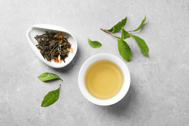 Photo of Cup of green tea, dry and fresh leaves on grey table, flat lay