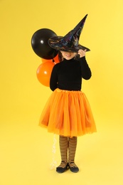 Cute little girl with balloons wearing Halloween costume on yellow background