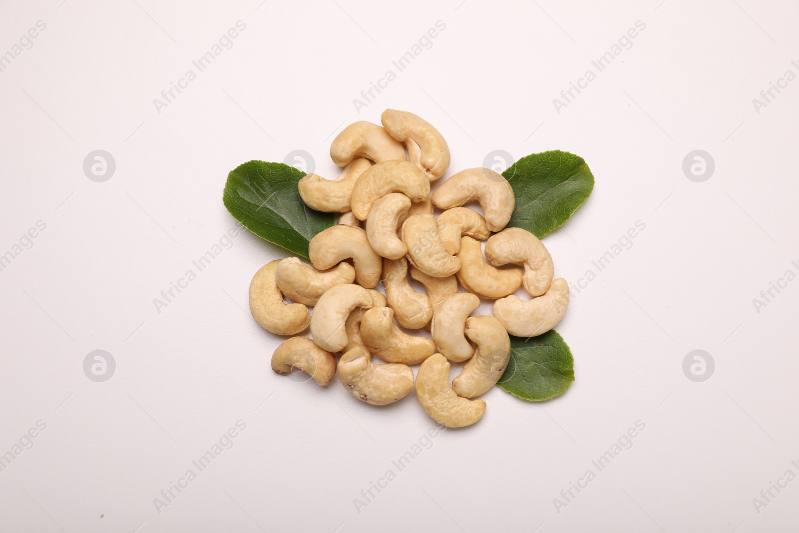 Photo of Pile of tasty cashew nuts and green leaves on white background, top view