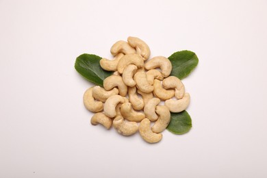 Pile of tasty cashew nuts and green leaves on white background, top view