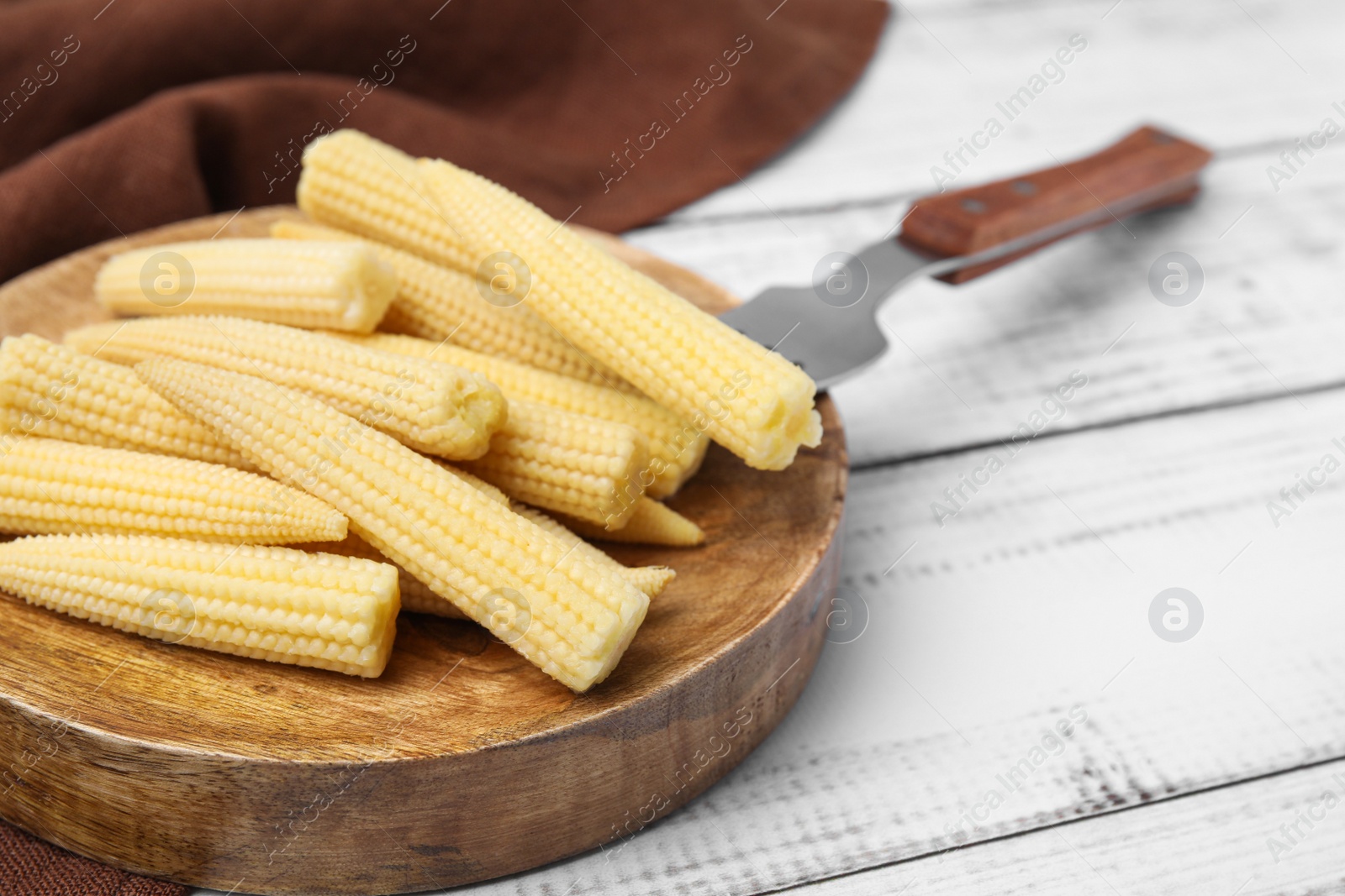 Photo of Pickled baby corn and fork on white wooden table, closeup. Space for text