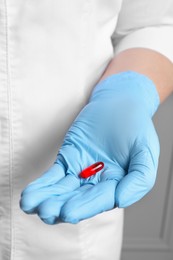 Photo of Doctor in medical glove holding pill on grey background, closeup