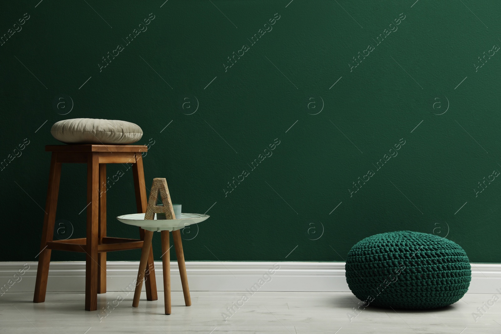 Photo of Stylish knitted pouf and wooden stool near green wall indoors, space for text