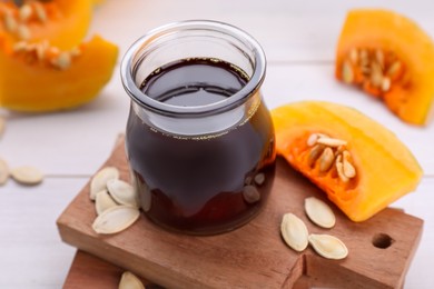 Photo of Fresh pumpkin seed oil in glass jar on white wooden table