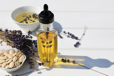 Healthy cooking oil, lavender flowers and pumpkin seeds on white wooden table, closeup. Space for text