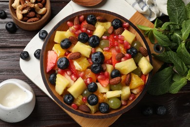 Photo of Delicious fruit salad in bowl, berries, nuts and fresh mint on wooden table, flat lay