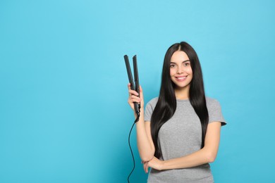 Photo of Beautiful happy woman with hair iron on light blue background. Space for text