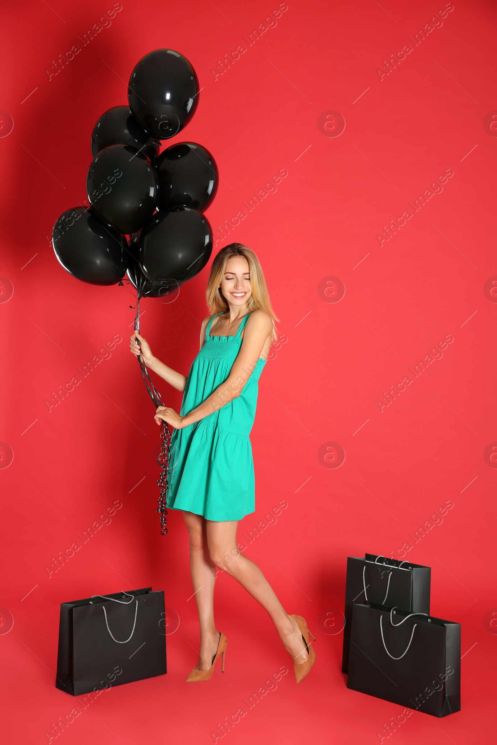 Photo of Happy young woman with balloons and shopping bags on red background. Black Friday Sale