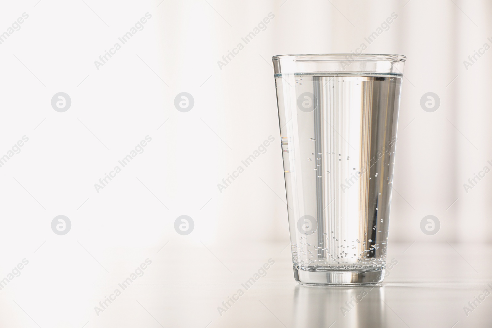 Photo of Glass with water on table against blurred background. Space for text