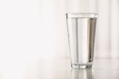 Photo of Glass with water on table against blurred background. Space for text