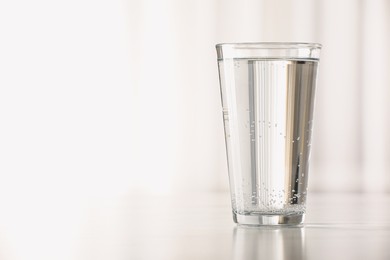 Glass with water on table against blurred background. Space for text