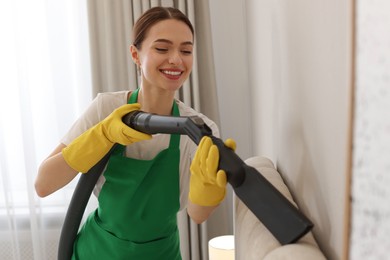Professional janitor in uniform vacuuming bed indoors