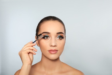 Portrait of young woman with eyelash extensions holding brush on light background
