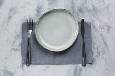 Photo of Empty plate, fork and knife on light grey table, top view