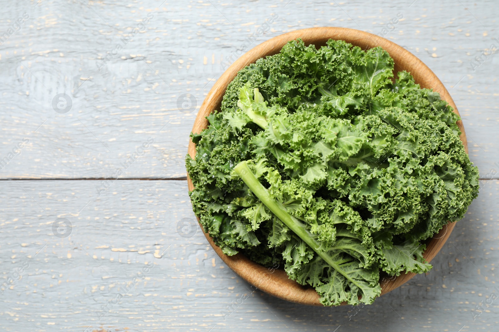 Photo of Fresh kale leaves on light grey wooden table, top view. Space for text