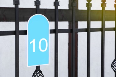 Photo of Plate with house number ten hanging on iron fence outdoors