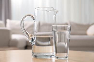 Photo of Jug and glass with clear water on table indoors, closeup