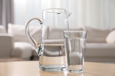 Jug and glass with clear water on table indoors, closeup