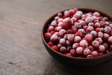 Photo of Frozen red cranberries in bowl on wooden table, closeup. Space for text