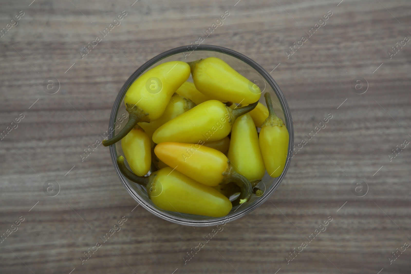 Photo of Glass bowl of pickled yellow jalapeno peppers on wooden table, top view