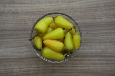 Photo of Glass bowl of pickled yellow jalapeno peppers on wooden table, top view