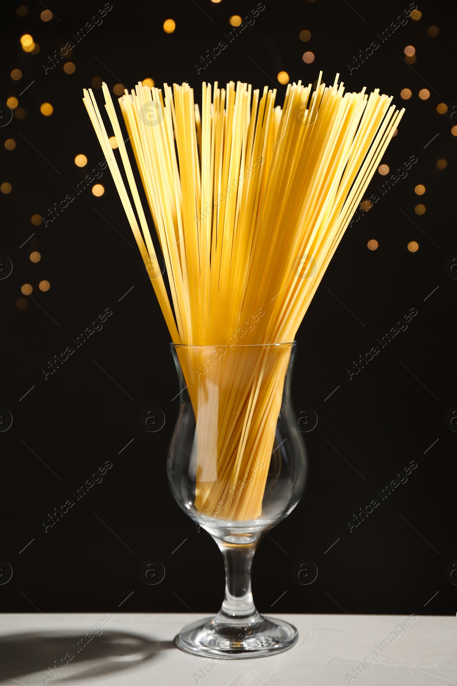 Photo of Uncooked spaghetti on grey table against blurred lights. Italian pasta