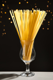 Photo of Uncooked spaghetti on grey table against blurred lights. Italian pasta