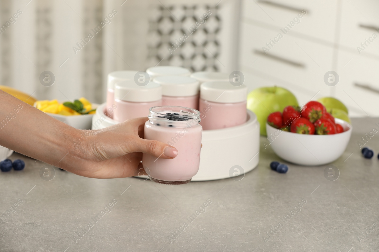 Photo of Woman holding jar of yogurt with blueberry over light grey table, closeup