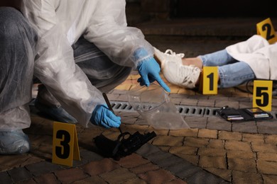 Criminologist in protective gloves working at crime scene with dead body outdoors, closeup