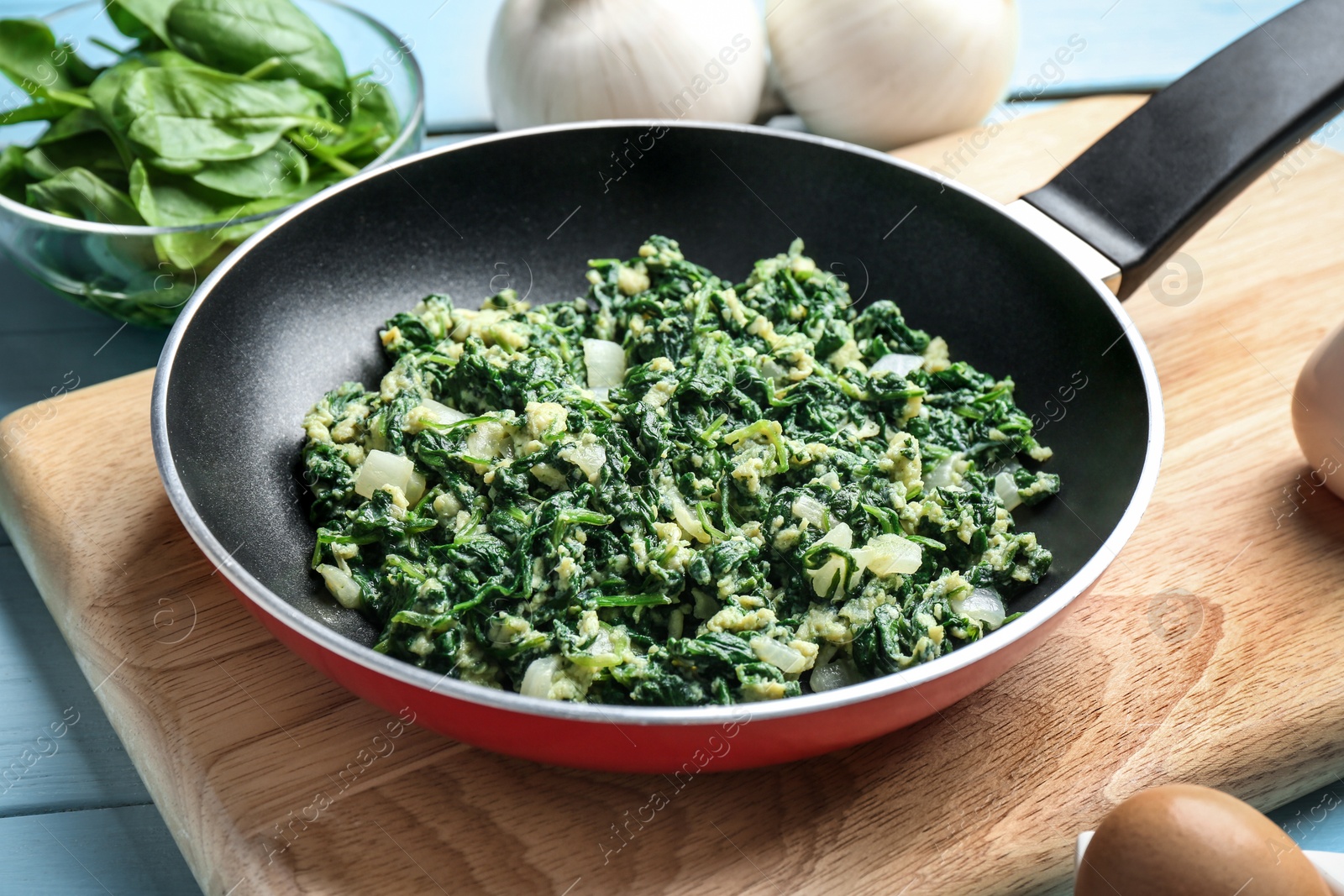 Photo of Tasty spinach in frying pan on light blue table. Healthy food