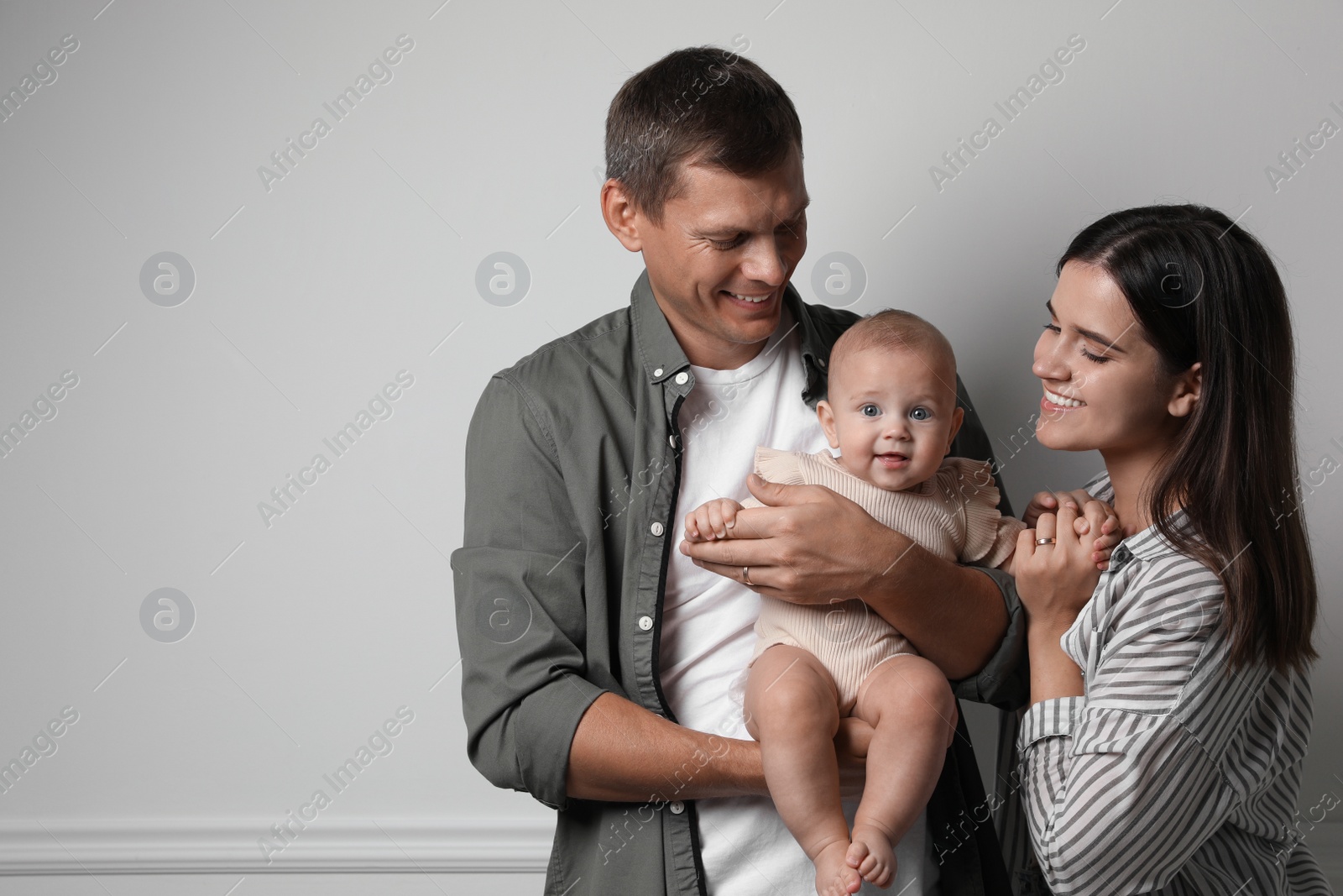 Photo of Happy family. Couple with their cute baby near light wall, space for text