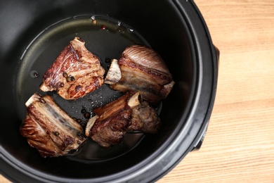 Photo of Delicious pork ribs in modern multi cooker on table, above view. Space for text