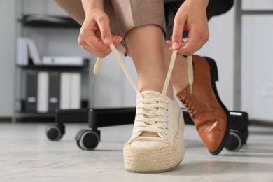 Woman taking off uncomfortable shoes and putting on sneakers in office, closeup