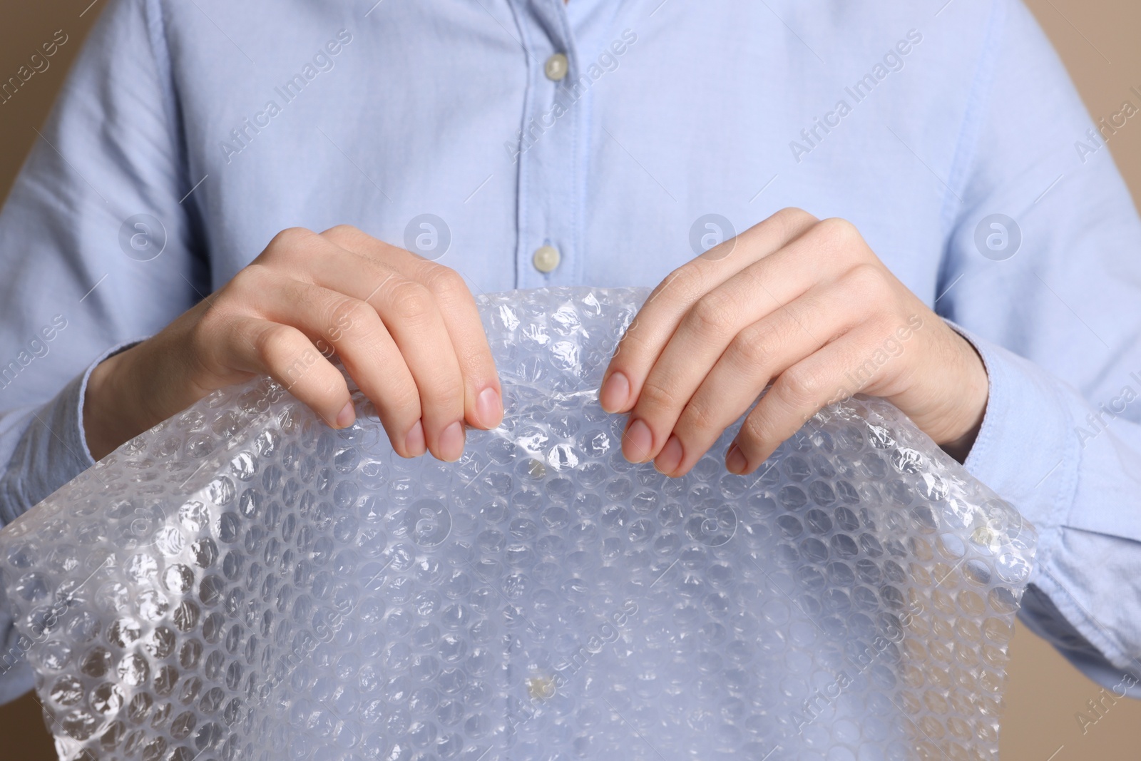 Photo of Woman popping bubble wrap on beige background, closeup. Stress relief
